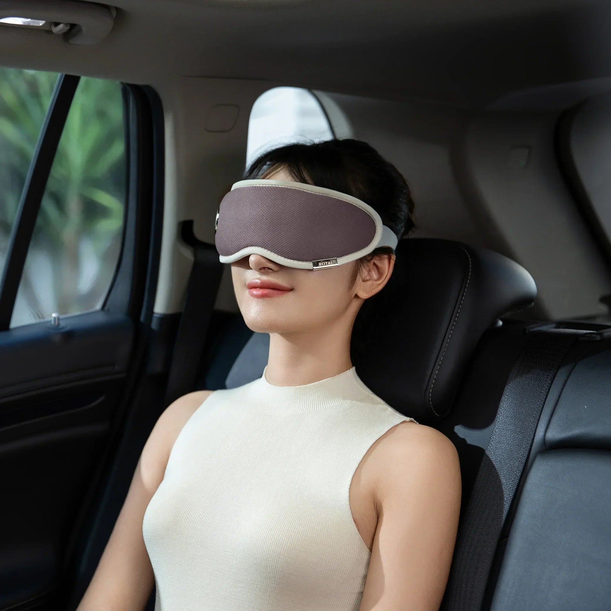 Woman relaxing in car backseat wearing gray eye mask and sleeveless cream top