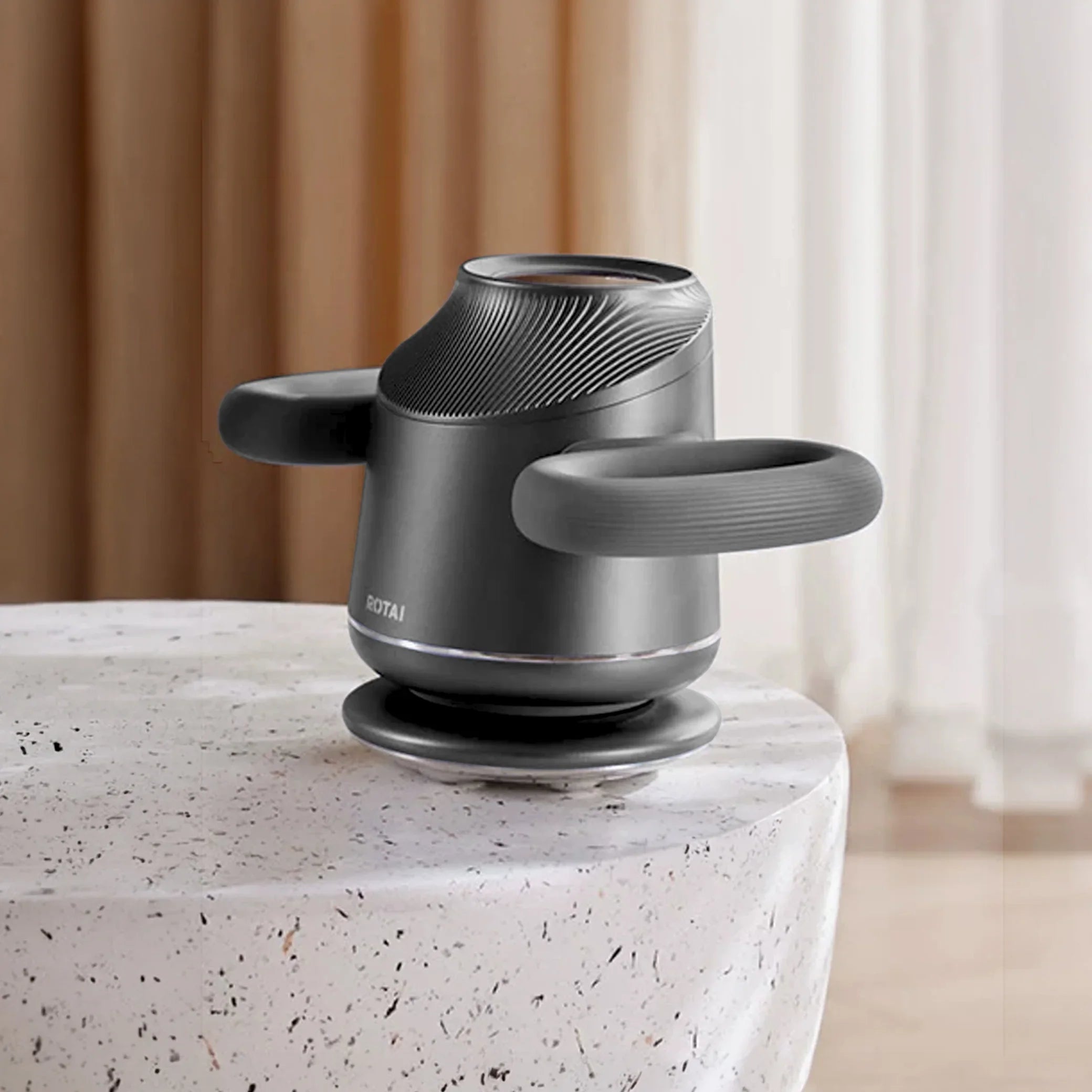 Modern handheld electric massager with dual handles on a marble table in a home setting
