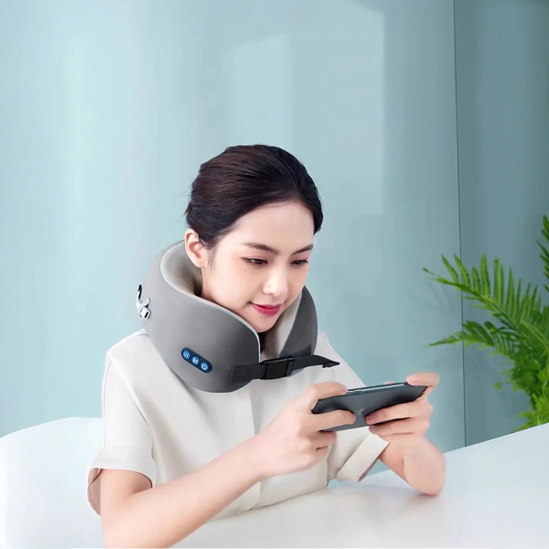 Woman using portable massage neck pillow while playing on smartphone in modern room