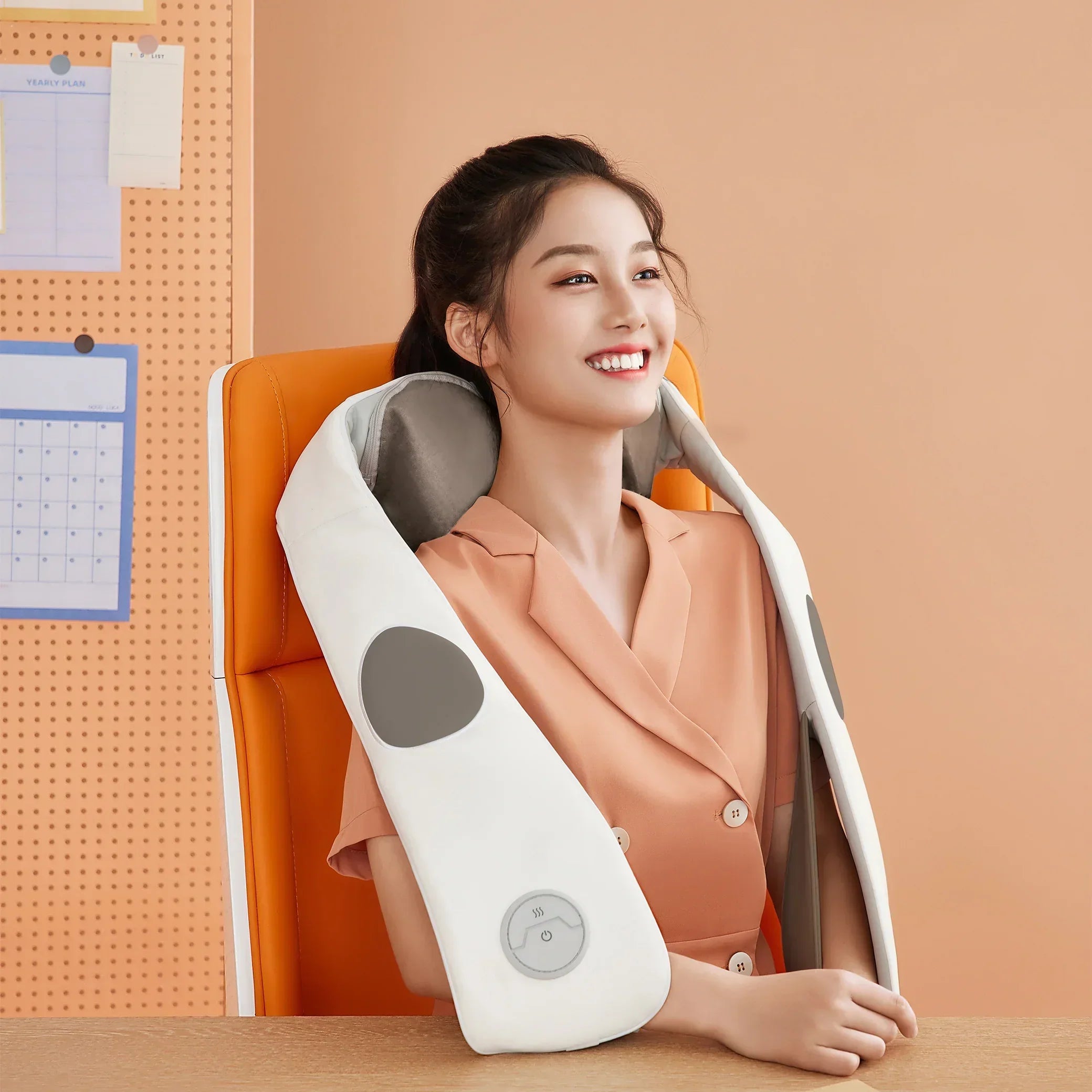Smiling woman in peach outfit using white and gray neck and shoulder massager on orange chair