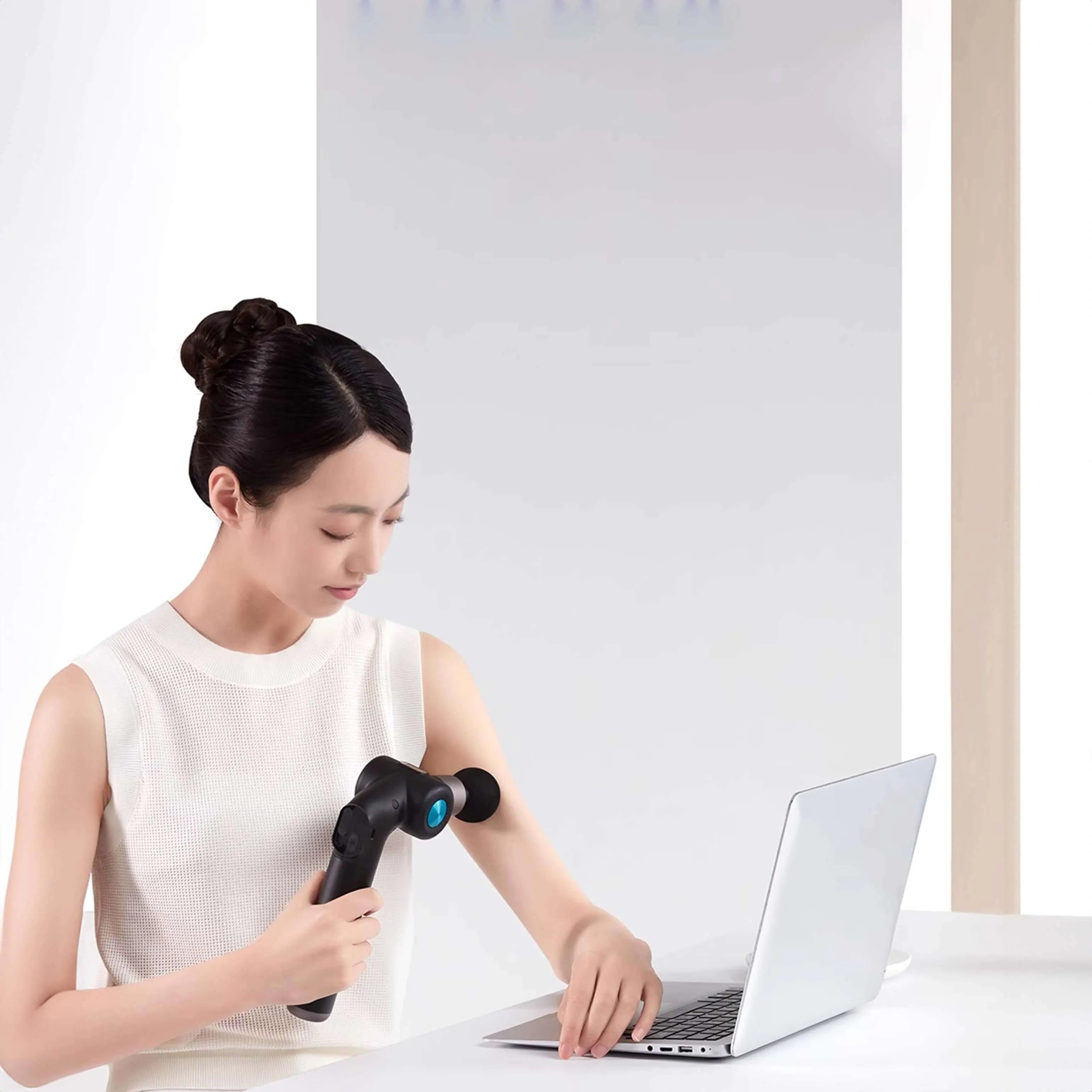 Woman using Rotai Muscle Therapy Foldable Massage Gun while working on laptop