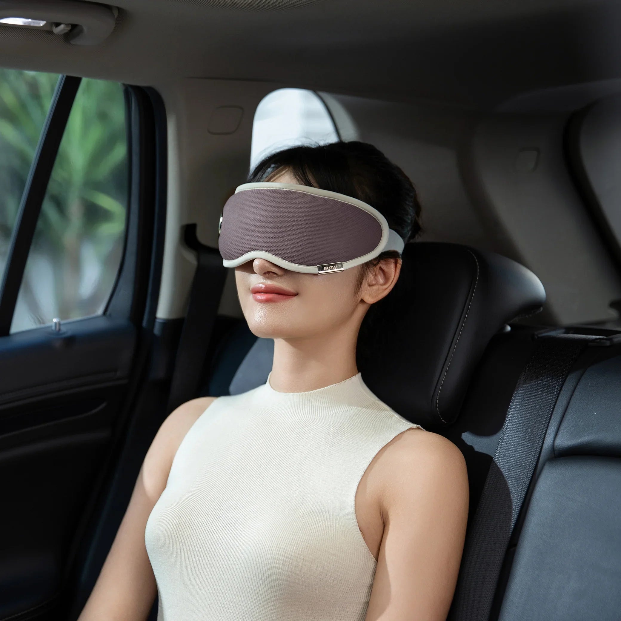 Woman relaxing in car backseat wearing gray eye mask and sleeveless cream top
