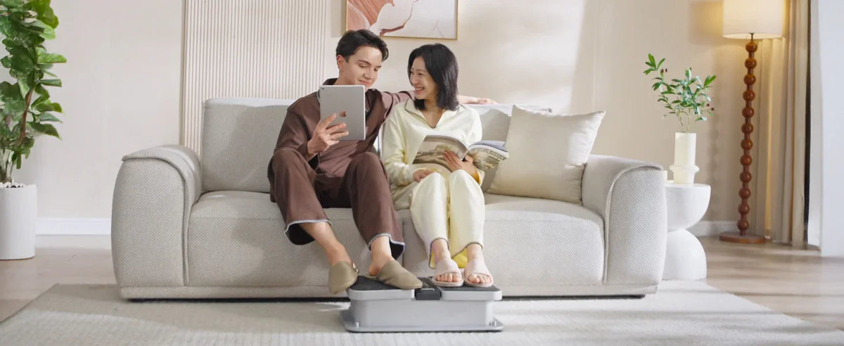 Couple relaxing on sofa using a foot massager, reading and browsing tablet in cozy living room