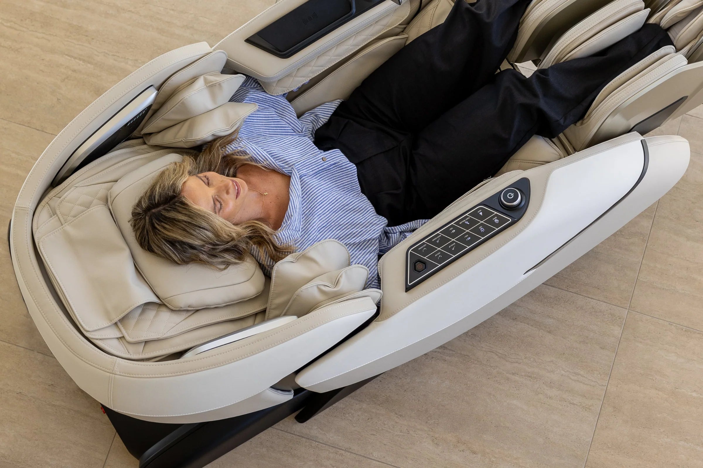 Woman relaxing in a beige full body massage chair with control panel, enjoying comfort and luxury.