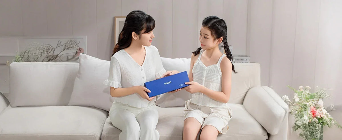 Woman and girl on sofa holding a blue Rotai massage product box in a bright living room