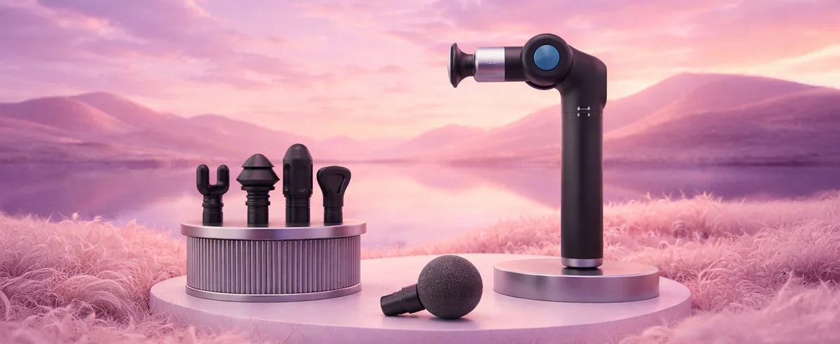 Foldable massage gun with interchangeable heads displayed outdoors on a pink scenic background